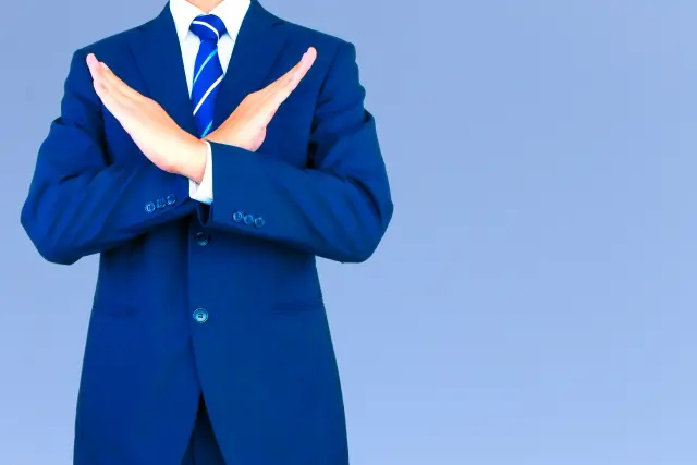 腕でバツ印を作るスーツの男性